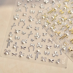 Macro detail of 3D bow nail stickers with gold and silver finishes and pearls