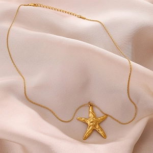 Macro detail of a 18K gold-plated starfish pendant on soft pink satin fabric
