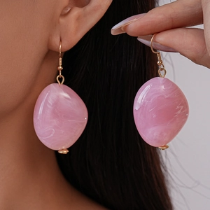 Detail of pink marble resin oval earrings with gold hooks worn by a model