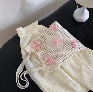 Close-up of cream knit hollow tote bag featuring decorative pink knitted bows