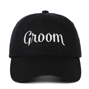 Detailed close-up of white Groom cursive embroidery on a black cotton baseball cap