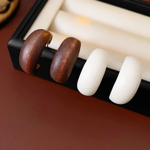 Detailed macro view of dark brown wood grain and white C-shaped hoop earrings in jewelry box