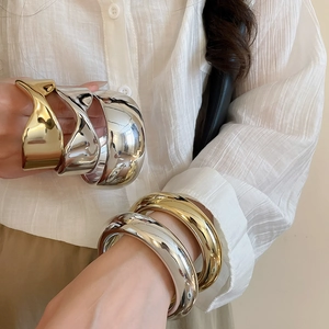 Close-up of minimalist gold and silver wide bangles with smooth and textured finishes