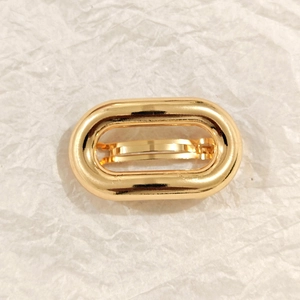 Detailed close-up of a high-polish oval gold metal hair clip on a white textured background