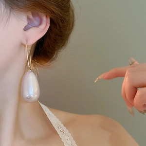 Dettaglio di un grande orecchino a goccia con perla crema su una modella