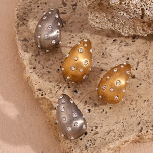 Détail macro de boucles d'oreilles goutte dorées brossées avec perles blanches