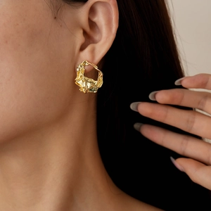 Close-up of gold irregular geometric wrinkled earrings worn by a model in soft lighting