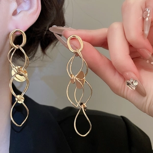 Detailed view of layered golden geometric wave tassel earrings worn on a model ear