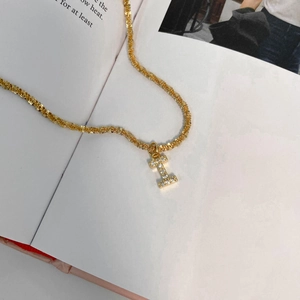 Détail macro du collier chaîne dorée torsadée avec pendentif lettre I serti de diamants brillants