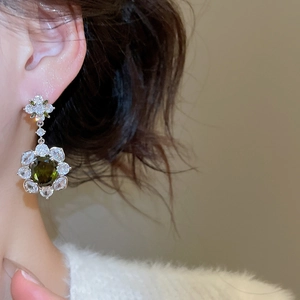Close-up of a floral earring with an oval green gemstone and sparkling zircons