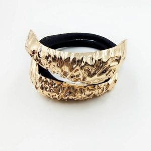 Detailed macro of gold alloy hair tie with irregular hammered texture on black elastic band