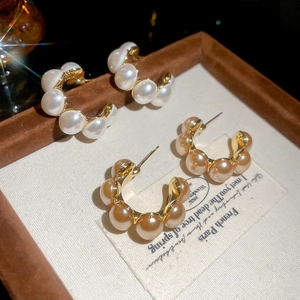 Gold plated C-shaped pearl stud earrings in white and champagne displayed in a velvet box