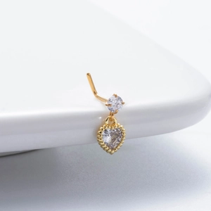 Detailed view of gold L-shaped nose stud with zircon heart pendant on white ceramic