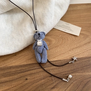 Détail du pendentif ours en denim avec perles et breloques étoiles sur un tricot blanc
