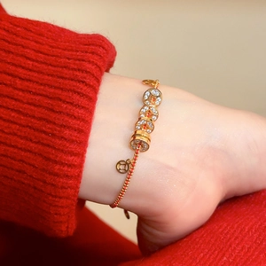 Gros plan de pièces dorées serties de cristaux sur un bracelet tressé rouge
