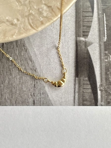 Detail of a minimalist gold croissant pendant necklace on a textured ceramic plate