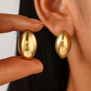 Macro shot of polished gold olive-shaped stud earring shown in hand and on ear