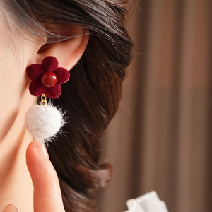 Detail of red velvet flower earring with fluffy white pom pom on a model's ear
