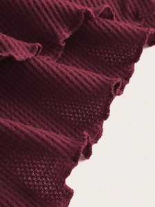 Detail shot of waffle knit fabric featuring ruffled wavy edges in a rich deep red hue