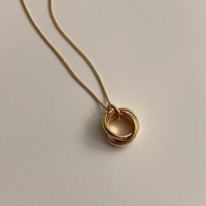 Detailed view of interconnected triple-ring gold pendant necklace on a minimalist background