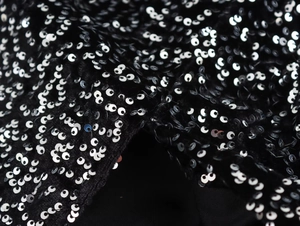 Macro detail of shimmering silver sequins sewn on premium black fabric for an asymmetric dress