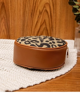 Close-up of leopard print round crossbody bag with brown leather and gold zipper detail
