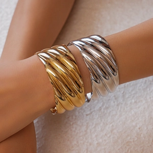 Detail view of gold and silver metallic wide cuff bracelets with wave texture on wrist