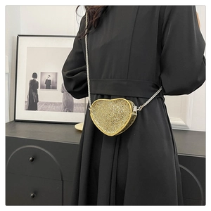 Detail of a sparkling golden heart-shaped crossbody bag with a fine metal chain strap