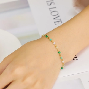 Detail of gold beaded bracelet with green and white square zircons on woman's wrist