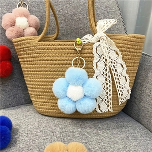 Close-up of colorful plush flower charms with gold metal clasps on a woven bag