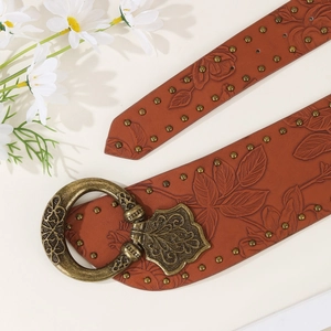 Brown punk leather belt with floral embossing and gold studs on a soft beige background