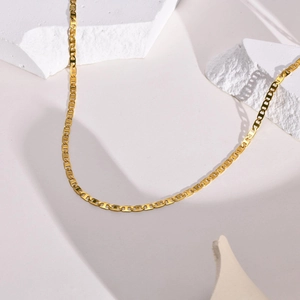 Detailed view of golden pig nose anchor link necklace on a white geometric plaster prop
