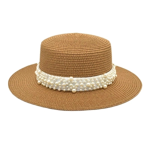 Détail d'un chapeau de paille marron avec ruban blanc orné de perles élégantes