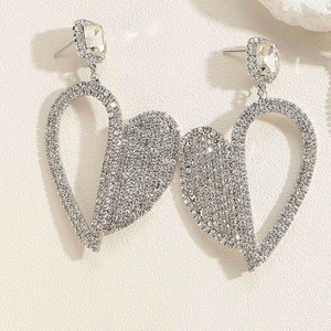 Detailed view of silver heart earrings featuring sparkling rhinestones on beige background