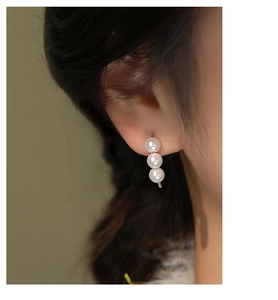 Detailed view of silver drop earrings featuring three vertically aligned white pearls on model