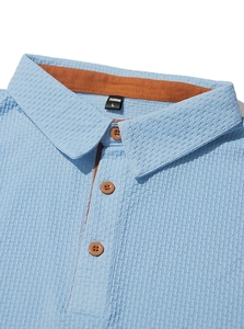 Détail d'un polo bleu clair à texture gaufrée avec doublure de col orange vif