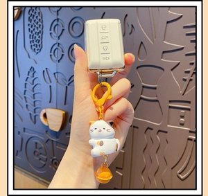 Close-up of white car key cover with cute cartoon cat and orange bell keychain accessory