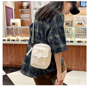 Close-up of a white bow-embroidered crossbody bag with a braided charm in a cozy cafe