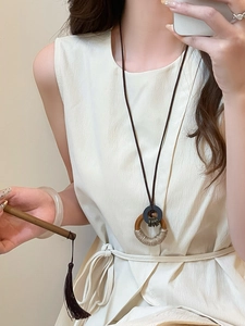 Retro ethnic style long necklace with circular wood and rope pendant on cream dress