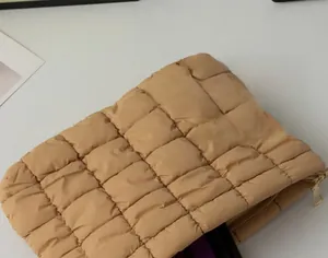 Macro shot of quilted puffer texture and zipper detail on light camel cosmetic bag
