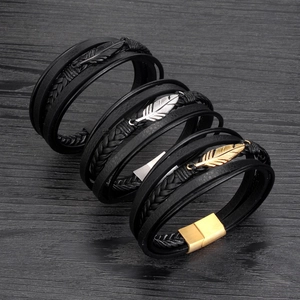Three men's multi-layer leather bracelets with feather metal charms on dark wood background