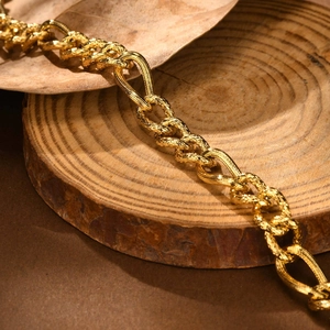 Gold stainless steel Figaro bracelet with textured round links and teardrop clasp on wood