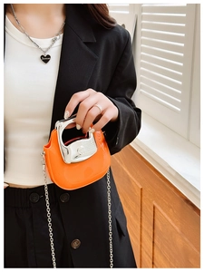 Detail of a bright orange mini crossbody bag with silver metal handle and chain strap