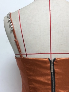 Detail eines orangen Metallic-Kleides mit silbernem Reißverschluss und Strass-Trägern