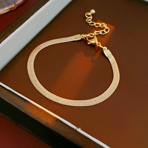 Macro shot of gold snake chain bracelet with fishbone texture and lobster clasp detail
