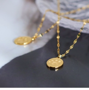 Close-up of golden round pendant with embossed paw print on a minimalist dainty chain