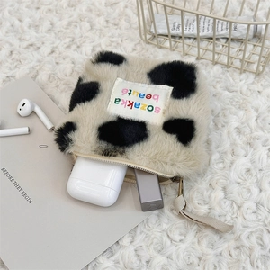 Detail of square cow print plush pouch with zipper closure and embroidered label