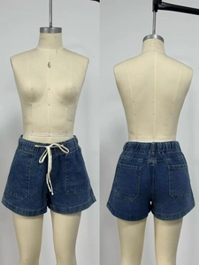 Detail of high waist drawstring and symmetrical pockets on blue wash denim shorts