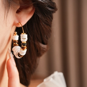 Primer plano de pendientes de aro en C con ojo de tigre y perlas en una modelo