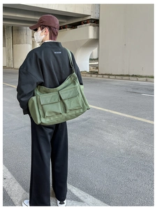 Rear view of a military green canvas crossbody bag worn by a model in urban setting